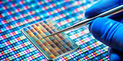 A detailed photo of a DNA microarray chip, used for genetic testing and research, with a scientist's hand manipulating the chip with tweezers.